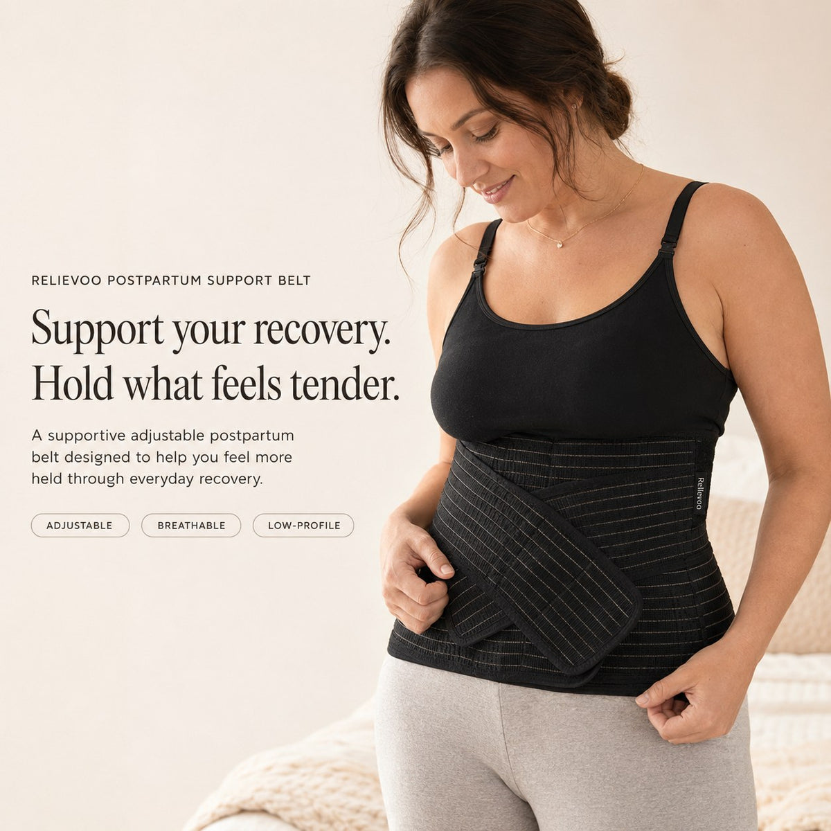 Woman wearing the black Relievoo postpartum support belt over a black vest top, holding the front support strap rvpumpen rvhasar