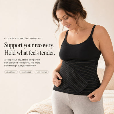 Woman wearing the black Relievoo postpartum support belt over a black vest top, holding the front support strap rvpumpen rvhasar