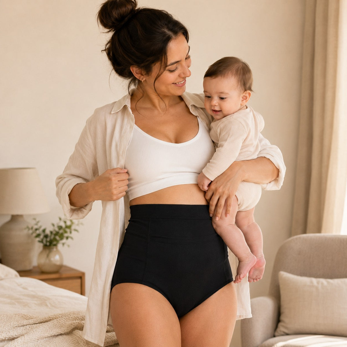 Mum wearing black Relievoo postpartum soothing briefs at home holding her baby