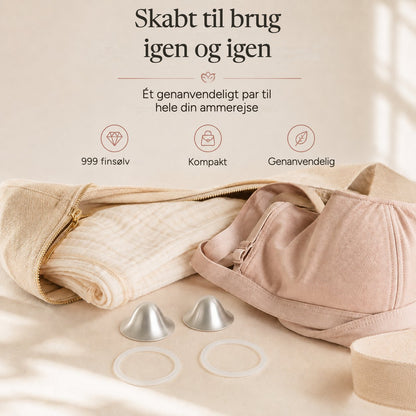 One reusable pair of silver nursing cups and two rings laid beside a folded muslin and a soft changing bag rvpumpen rvhasar