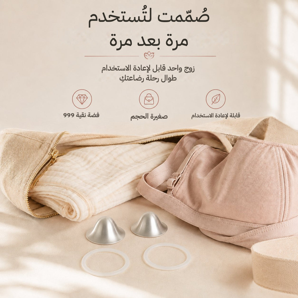 One reusable pair of silver nursing cups and two rings laid beside a folded muslin and a soft changing bag